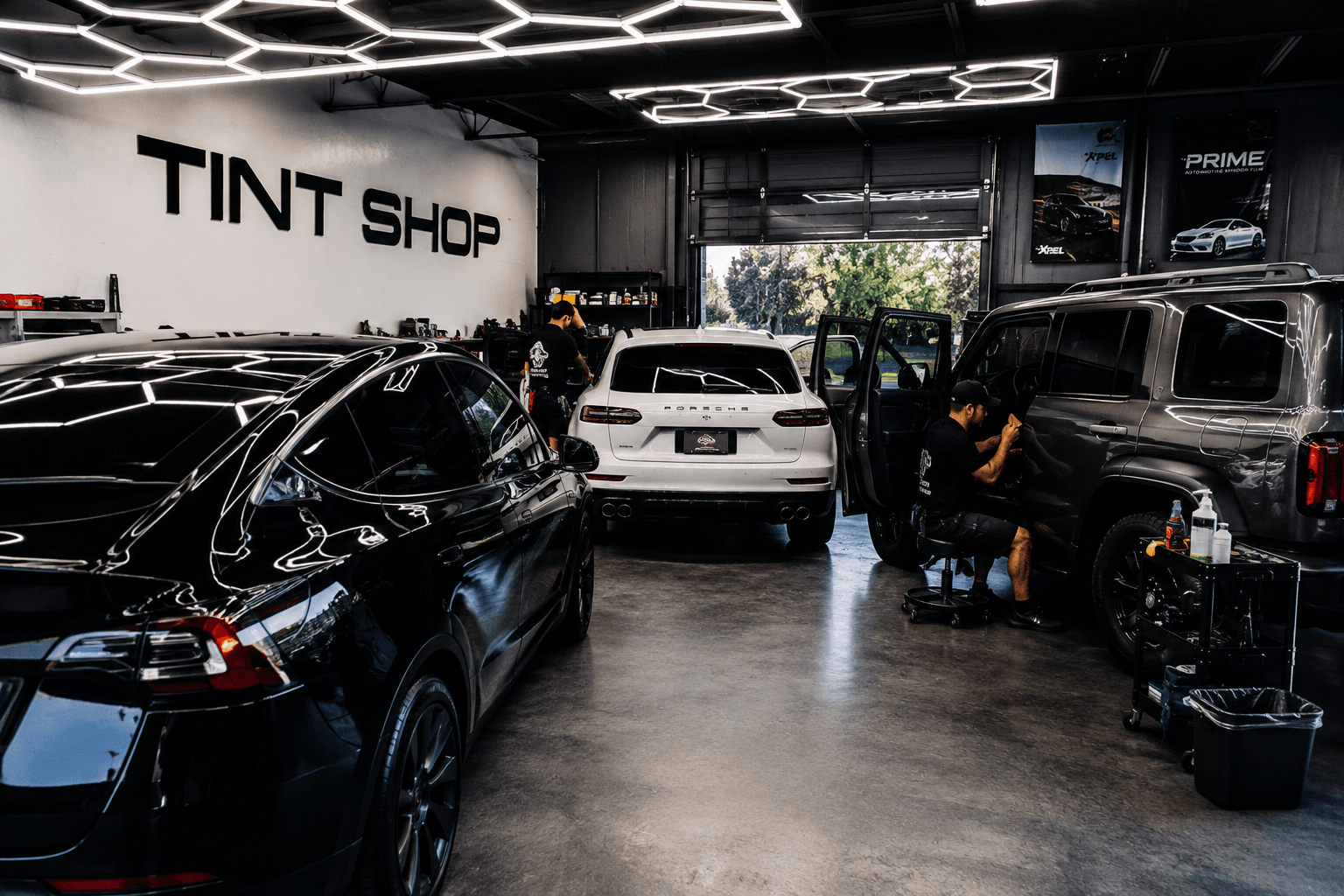 Busy tint shop interior with multiple vehicles being tinted including Tesla and Porsche