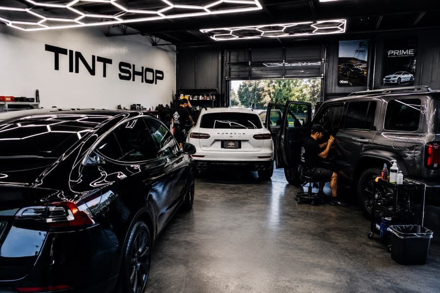 Busy tint shop interior with multiple vehicles being tinted including Tesla and Porsche